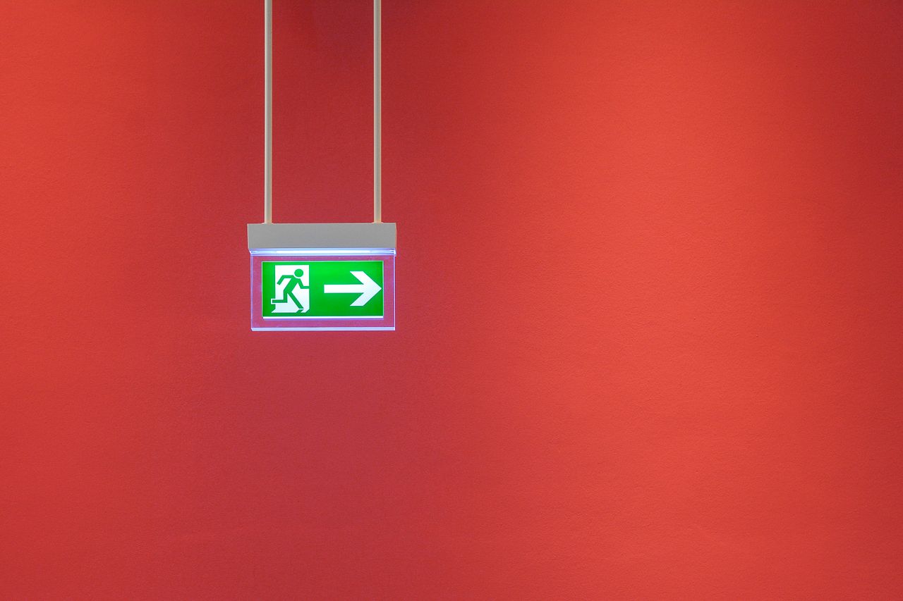 Green emergency exit sign with arrow on vibrant red wall, indicating direction for safety.