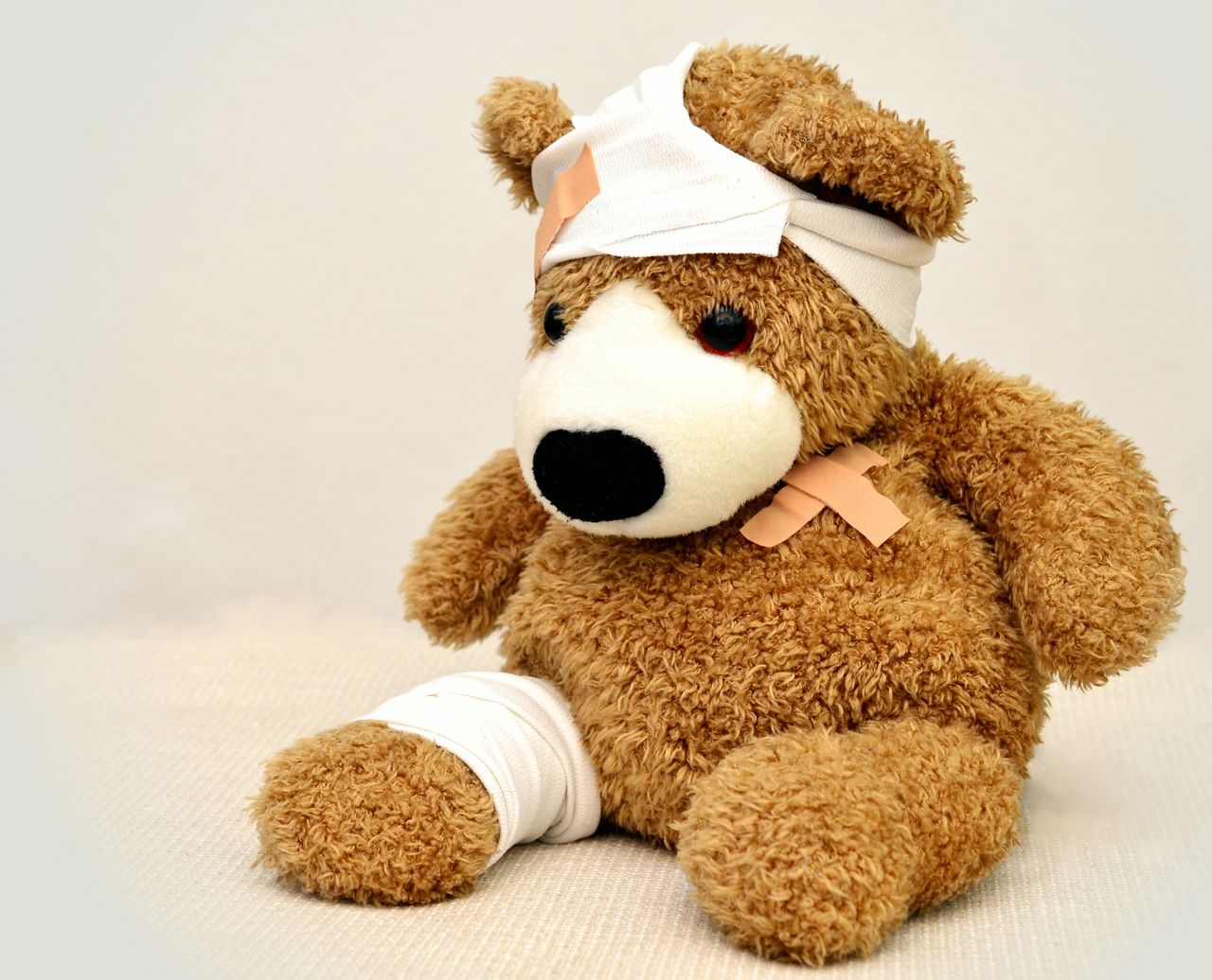 Home A brown teddy bear with bandages, depicting a playful take on injury recovery in a minimalist setting.